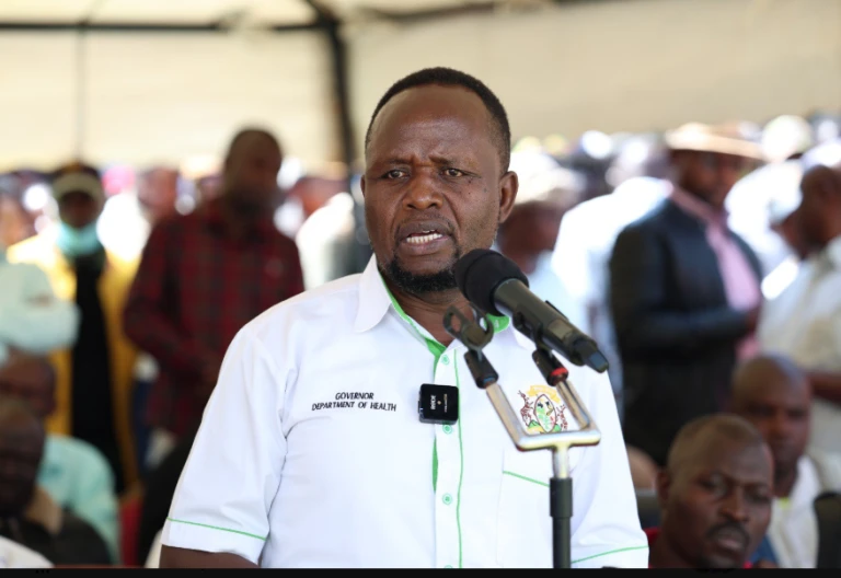 George Natembeya, wearing a white shirt with green trim, speaks at microphones.