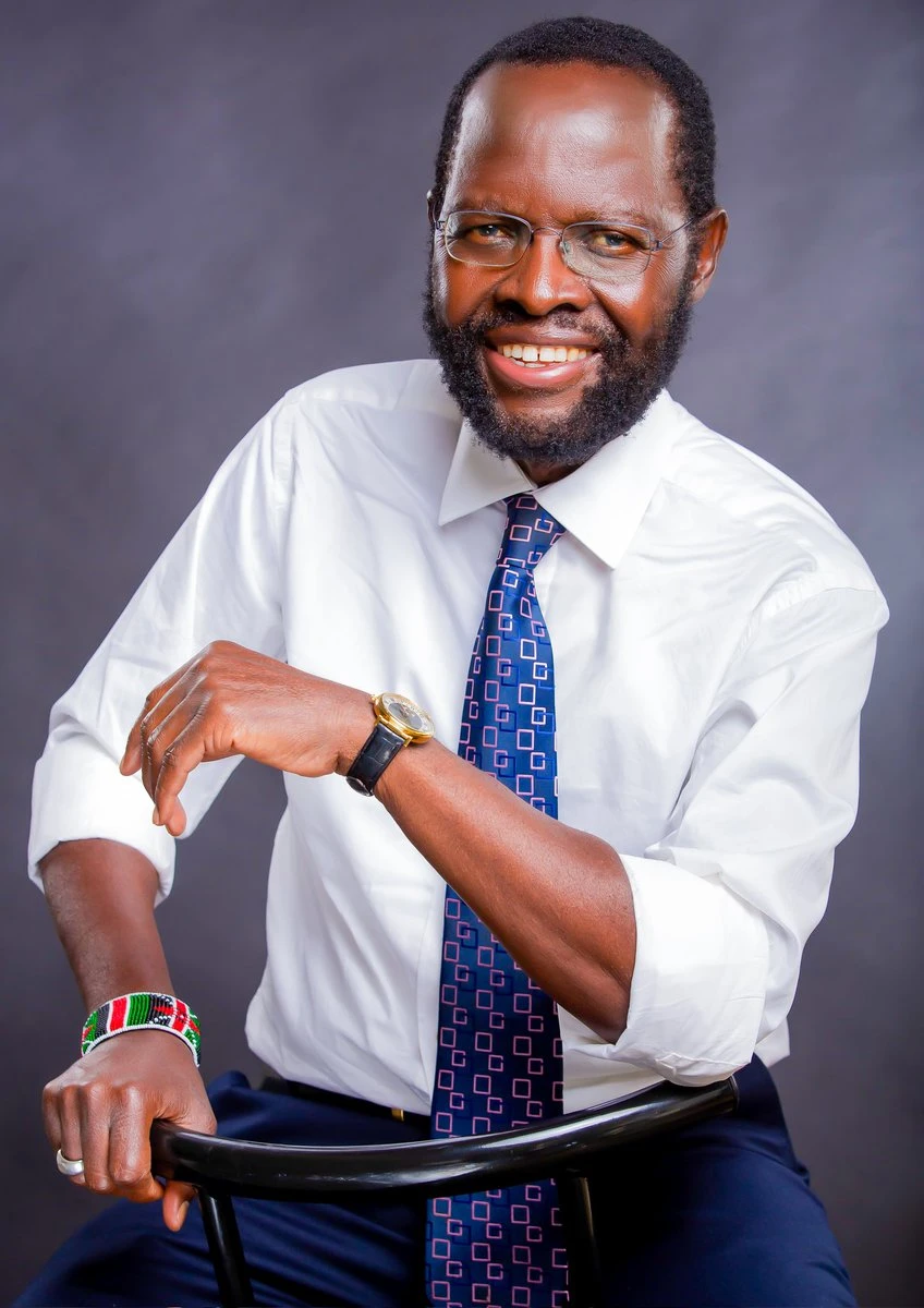 Anyang’ Nyong’o smiles in glasses, a white shirt and patterned blue tie.