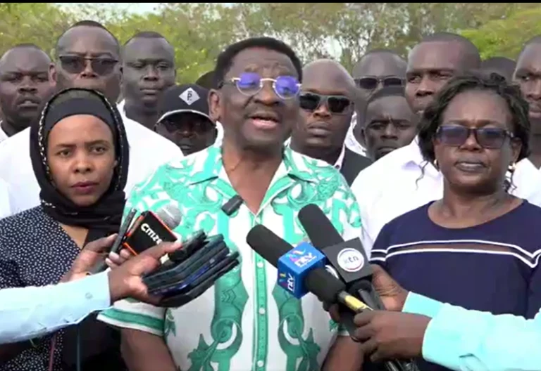 James Orengo speaks to reporters outdoors beside Ida Odinga and other attendees.