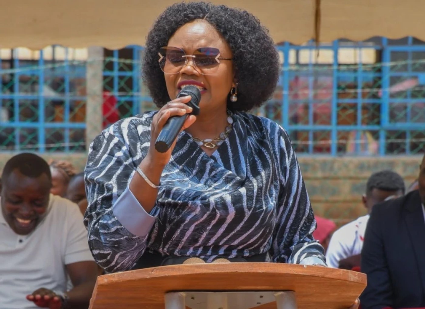 Githunguri MP Gathoni Wamuchomba speaks into a microphone at a lectern during an outdoor public event.