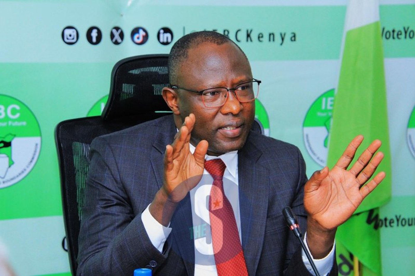 IEBC Chairperson Erastus Ethekon gestures while speaking in front of an IEBC backdrop.