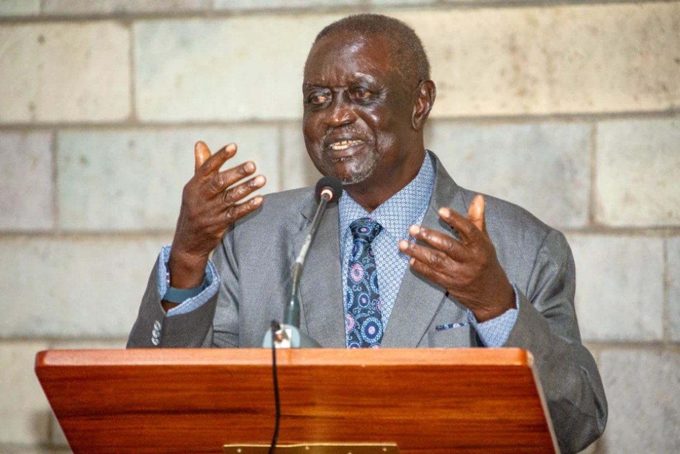 ODM leader Oburu Oginga, in a grey suit and patterned tie, gestures while speaking at a wooden lectern.