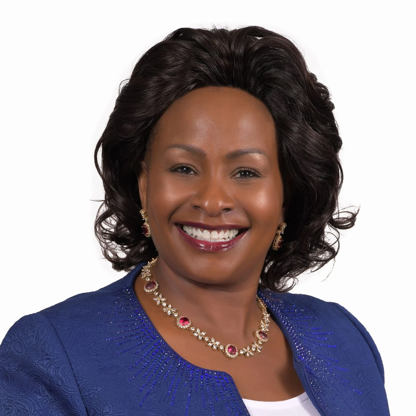 Wavinya Ndeti smiles in a blue jacket and gold necklace against a white background.