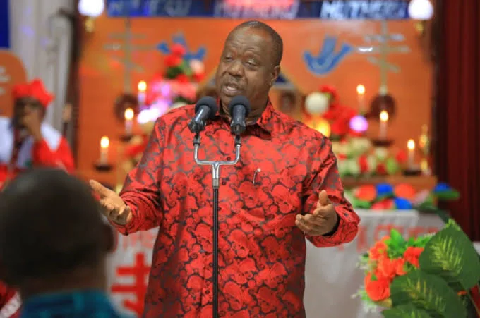 Fred Matiang’i speaks at microphones, gesturing with both hands.